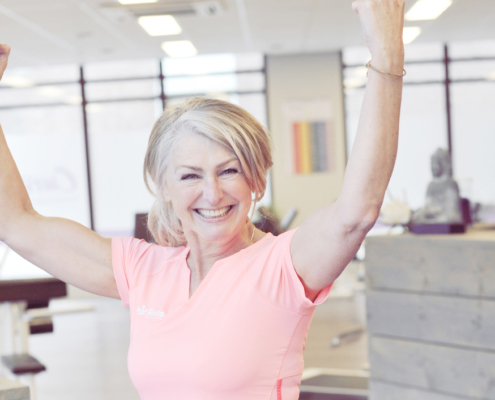 Sterke spieren krachttraining, 50+ vrouw traint met lichte gewichten in moderne fitnessruimte terwijl een coach haar begeleidt. Diverse vrouwen oefenen op hydraulische apparatuur in een warme, uitnodigende sfeer.
