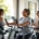 Diverse vrouwen trainen samen in lichte Curves-sportschool; één gebruikt krachtapparaat, ander doet cardio, terwijl coach begeleidt in uitnodigende circuitopstelling.