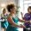 Twee diverse vrouwen trainen op hydraulische weerstandsmachines in een lichte Curves fitnessstudio, begeleid door een ondersteunende coach tijdens een 30-minuten circuittraining.
