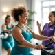 Twee diverse vrouwen trainen op hydraulische weerstandsmachines in een lichte Curves fitnessstudio, begeleid door een ondersteunende coach tijdens een 30-minuten circuittraining.