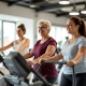 Vrouwen van 50+ trainen samen op paarse Curves-fitnessapparaten in een lichte, uitnodigende ruimte. Een coach begeleidt subtiel, in een toegankelijke, ondersteunende omgeving.