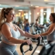 Vrouwen van 50+ trainen op Curves' hydraulische apparatuur in cirkelvormige opstelling, terwijl een coach vriendelijk begeleidt in een toegankelijke, ondersteunende fitnessomgeving.