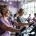 Diverse vrouwen trainen op hydraulische apparatuur bij Curves fitness, begeleid door een coach in een lichte, moderne ruimte met paarse accenten.