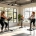 Vrouwen van verschillende leeftijden trainen samen op hydraulische apparaten in een lichte Curves-fitnessruimte, begeleid door een coach in een uitnodigende, ondersteunende sfeer.