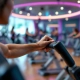 Vrouwenhand op hydraulisch weerstandsapparaat bij Curves-fitnesscircuit met paarse en turkooizen verlichting. Andere vrouwen trainen in een uitnodigende, moderne omgeving.