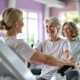Drie vrouwen van middelbare leeftijd trainen op hydraulische fitnessapparaten in een lichte studio, begeleid door een coach in een verwelkomende, inclusieve omgeving voor beginners.