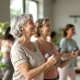 Diverse vrouwen van middelbare leeftijd doen krachttraining met lichte dumbbells in een lichte fitnessstudio, begeleid door een ondersteunende coach in een rustige, positieve sfeer.