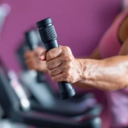 Gespierde arm van een vrouw die een hydraulische weerstandsmachine gebruikt in een Curves fitnesszaal met paarse en roze accenten.