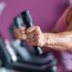 Gespierde arm van een vrouw die een hydraulische weerstandsmachine gebruikt in een Curves fitnesszaal met paarse en roze accenten.
