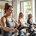 Diverse vrouwen trainen samen in een lichte Curves fitnessstudio, waarbij een coach begeleiding biedt bij het gebruik van hydraulische weerstandsapparatuur in een warme, veilige omgeving.