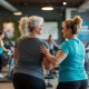 Twee 50+ vrouwen trainen op hydraulische apparatuur in een Curves fitnesszaal, begeleid door een vriendelijke coach in ondersteunende sfeer.
