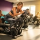 Vrouw van middelbare leeftijd stelt gewichtsplaten in op hydraulische weerstandsmachine in helder verlichte fitnessstudio