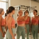 Diverse groep vrouwen van middelbare leeftijd bekijkt spiegelbeeld in moderne sportschool, één vrouw toont zelfverzekerd armspieren