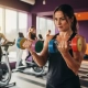 Vastberaden vrouw van middelbare leeftijd traint met kleurrijke dumbbells in heldere fitnessstudio met andere vrouwen op achtergrond