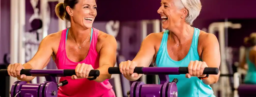Twee vrouwen van middelbare leeftijd lachen tijdens krachttraining op paarse hydraulische machines in een levendige damesfitnesclub.