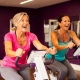 Twee vrouwen van middelbare leeftijd trainen lachend op hydraulische fitnessmachines in een paars ingerichte damesfitnessstudio.