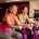 Twee vrouwen lachen samen tijdens een krachttraining op paarse hydraulische fitnessapparaten in een vrouwenfitnessclub.