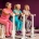 Drie vrouwen van 50-60 jaar lachen en sporten samen op hydraulische fitnessapparaten in een paarse damesfitnessruimte.