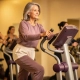 Vrouw van middelbare leeftijd stapt vastberaden op een Curves hydraulisch fitnessmachine in een warm verlichte sportschool.