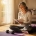 Vrouw van middelbare leeftijd met grijs haar schrijft in wellness-dagboek op yogamat bij zonnig raam, kleine halter naast haar.